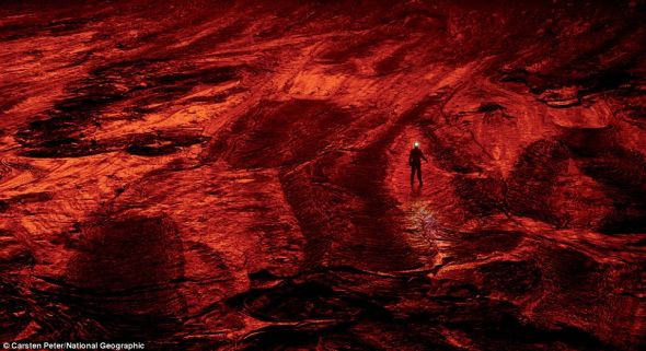 一名探索队成员正在火山口变凉的熔岩地面上行走，在熔岩湖发出的光线的映衬下，这片熔岩呈现出可怕的红色