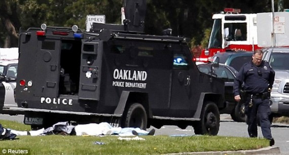 A police armored vehicle drives by what appears to be covered dead bodies following the gun attack