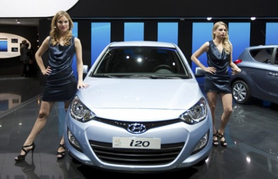 Hostesses stand next to a Hyundai i20 model car displayed on the car maker's booth during the first media day of the Geneva Auto Show at the Palexpo in Geneva