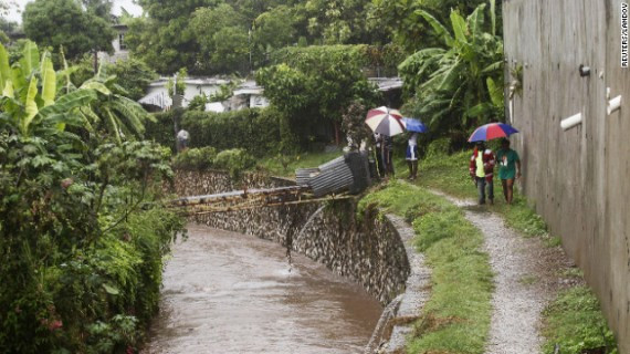 Jamaicans shelter themselves from the rain of approaching Hurricane Sandy as they walk along the Hope River on Wednesday.