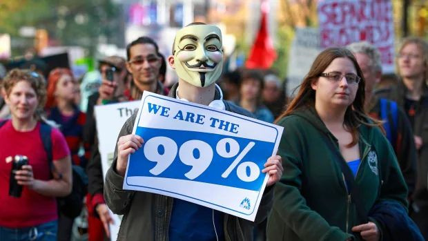 A man holds up a protest sign as he marches with thousands of people through the streets participating in the Occupy Vancouver protest on Oct.15, 2011. A new report called 'An Economy for the 99%' paints a stark picture of wealth inequality in Canada and around the world.