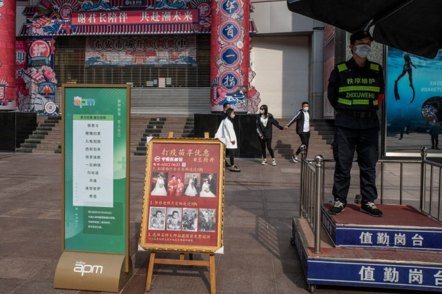 北京一个打疫苗享优惠布告牌边，一家国有照相馆打出了为接种新冠疫苗者拍婚纱照享九折优惠的广告。