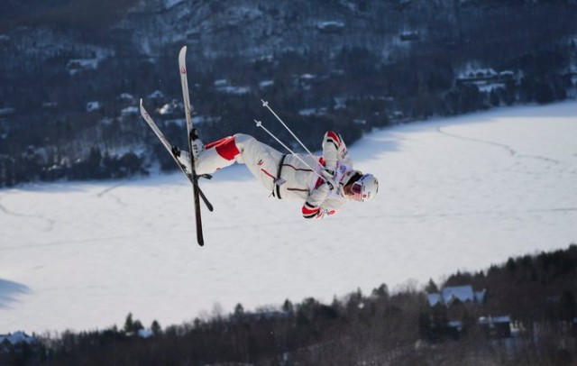 A freestyle skier performing a mid-air flip at the 2022 World Cup in Mont Tremblant, Que. A second ski hill, and snowy, mountainous forests are seen in the background far below the skier.