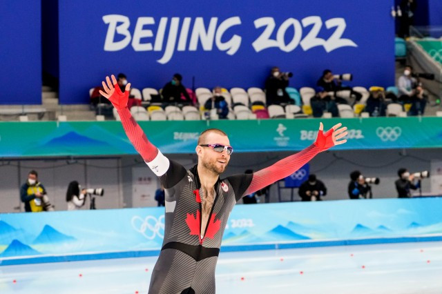 A photo of a speed skater with his hands up in the air smiling