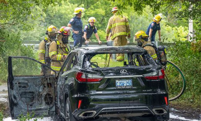 Firefighters stand near a black Lexus SUV that was badly damaged by fire