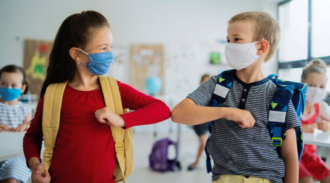 Small children with face mask back to school, greeting each other with an elbow bump