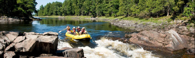 four people rafting in river surrounded by forest about to go down rapids