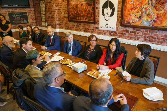 A woman is sitting at a table and speaking. On the other side of the table, Prime Minister Justin Trudeau is leaning forward and listening. Member of Parliament Terry Duguid and other people are also sitting around the table.