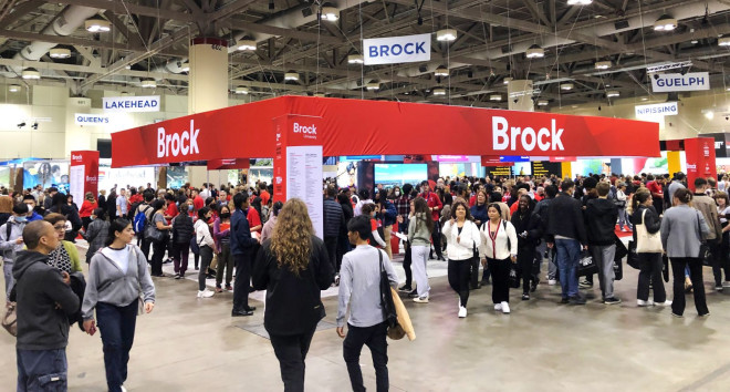 Crowds of people walk in and around a Brock University display area.