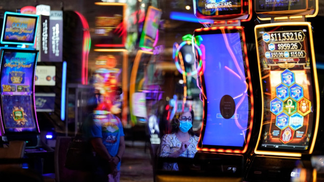 A woman, wearing masks as a precaution against the coronavirus, plays an electronic slot machine during the reopening of the Mirage hotel and casino, Thursday, Aug. 27, 2020, in Las Vegas. The casino closed earlier this year due to the coronavirus outbreak. (AP Photo/John Locher)