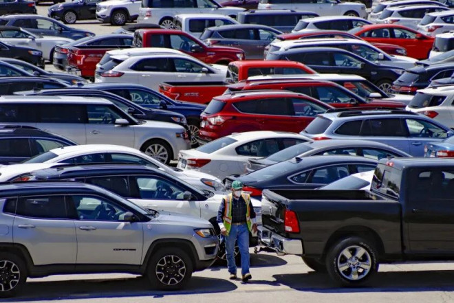 A worker walks through vehicles stored in the lots at the Cox Automotive Inc. Manheim Pittsburgh vehicle auctioning location in Cranberry Township, Pa., Wednesday, May 13, 2020. The corporation announced earlier this week it will furlough workers at the location and more at its other locations around the country due to the COVID-19 pandemic. (AP Photo/Keith Srakocic)