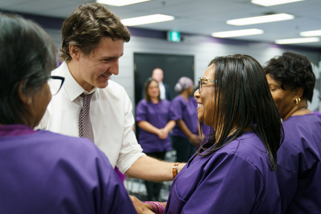 Prime Minister Justin Trudeau shakes hands with a personal support worker who is wearing scrubs. Other people are standing beside them.