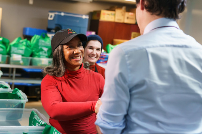 Le premier ministre Justin Trudeau est debout devant deux bénévoles à la banque alimentaire Projaide. Les deux bénévoles sourient.
