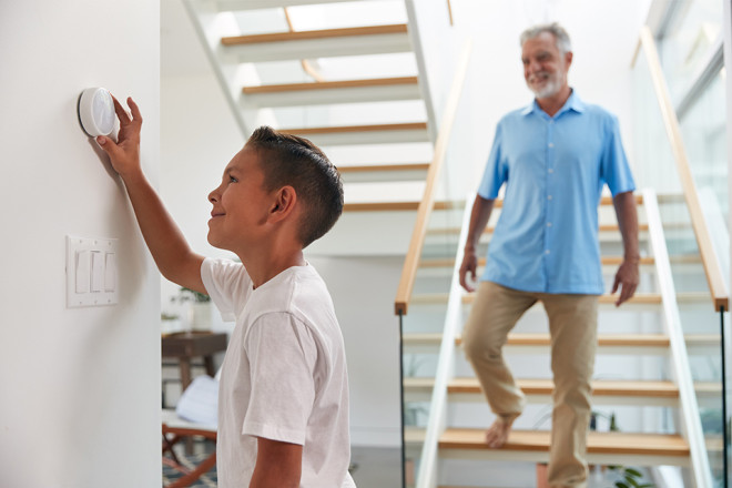 father watching son set smart thermostat