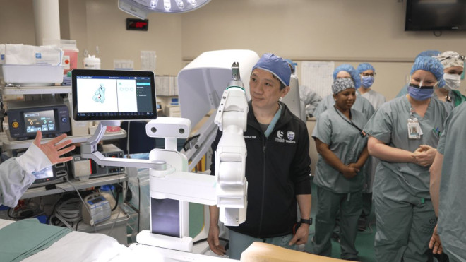 A surgeon stands behind a medical robot in an operating room.