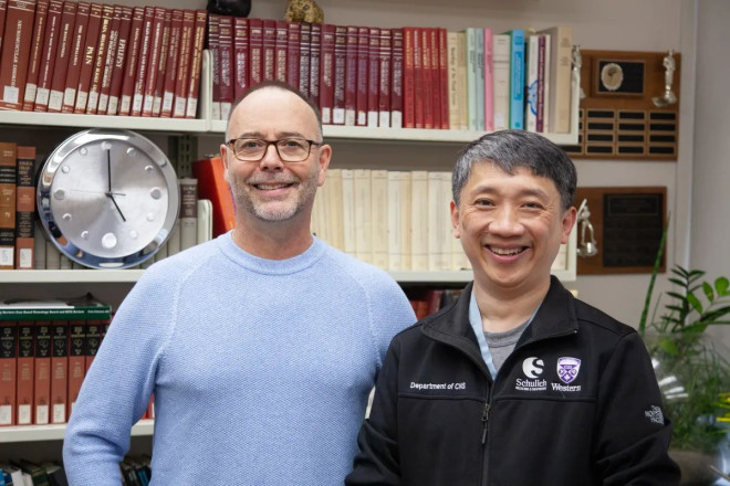 Two men smiling in front of a bookshelf in an office.