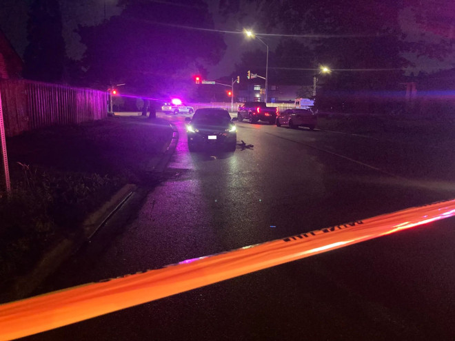 A dark intersection with a police vehicle and a dark-coloured car with caution tape in the foreground.