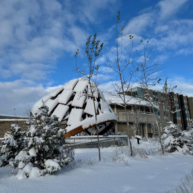 Wampum Learning Lodge's Ceremonial Arbour is covered in a fresh layer of snow. A small, snowy pine is in the foreground.