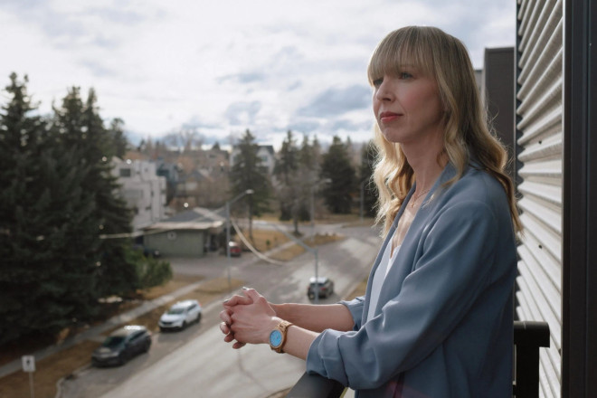 A woman with blond hair, wearing a blue shirt and looking off into the distance