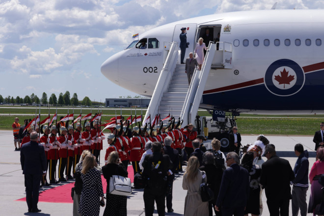 Their Majesties King Charles III and Queen Camilla coming down the steps of an airplane.