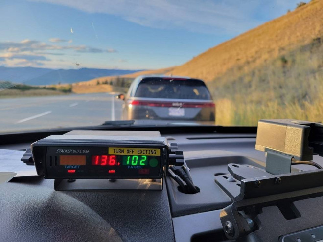 A police radar reads 136 km/h in front of a grey minivan stopped at the side of the highway