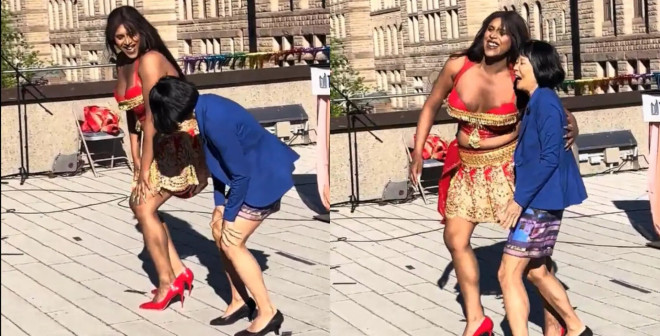 一位身穿彩色裙子、红高跟鞋的女性在户外和两名儿童共舞,背景为阳光明媚的都市历史建筑。